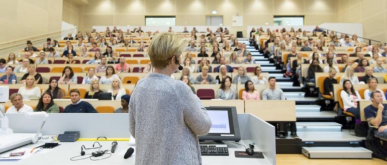 Bilde av underviser med ryggen til kamera foran en full sal.