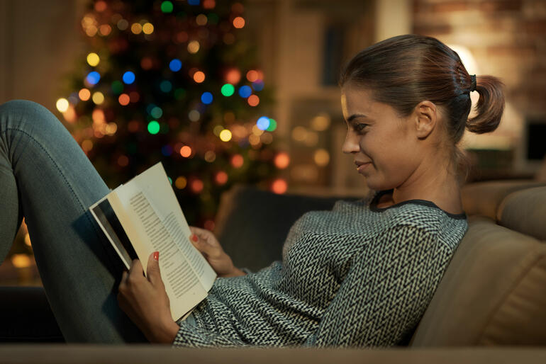Ung kvinne leser foran juletreet